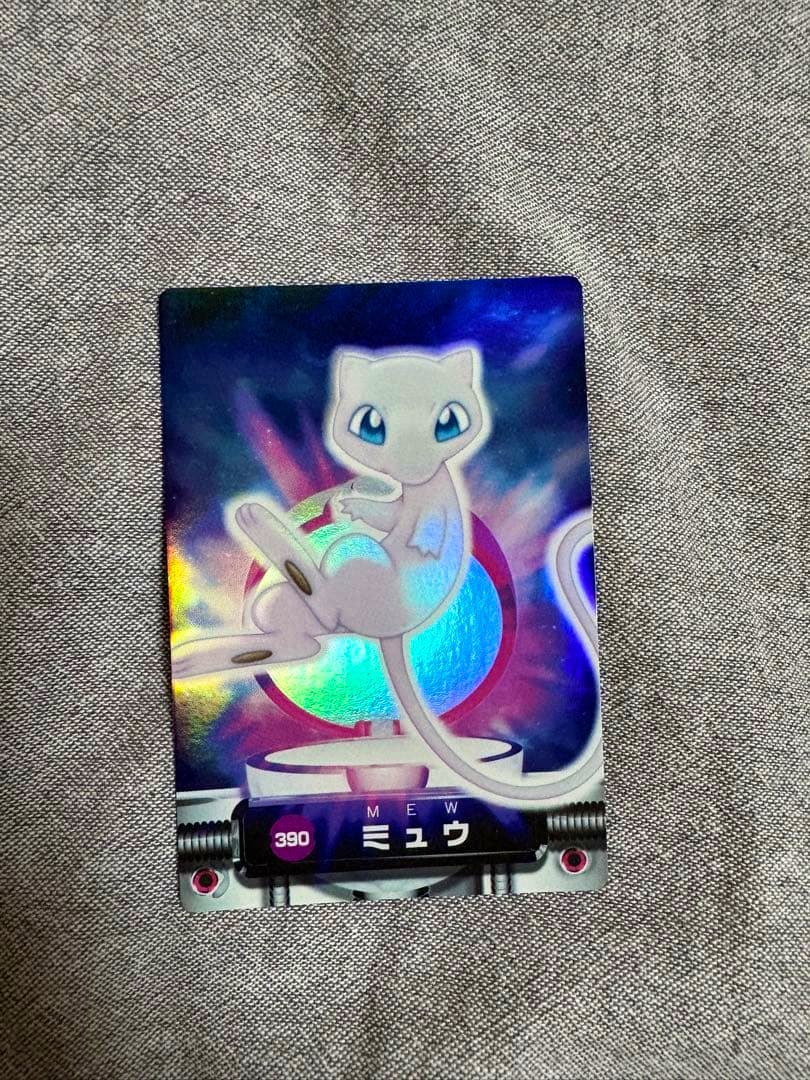 Front of a holographic Pokémon trading card showing Mew and the number 390 on a fabric surface.