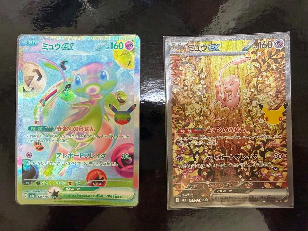 Two Pokémon trading cards (Mew ex) front faces in protective sleeves shown side-by-side on a dark surface.