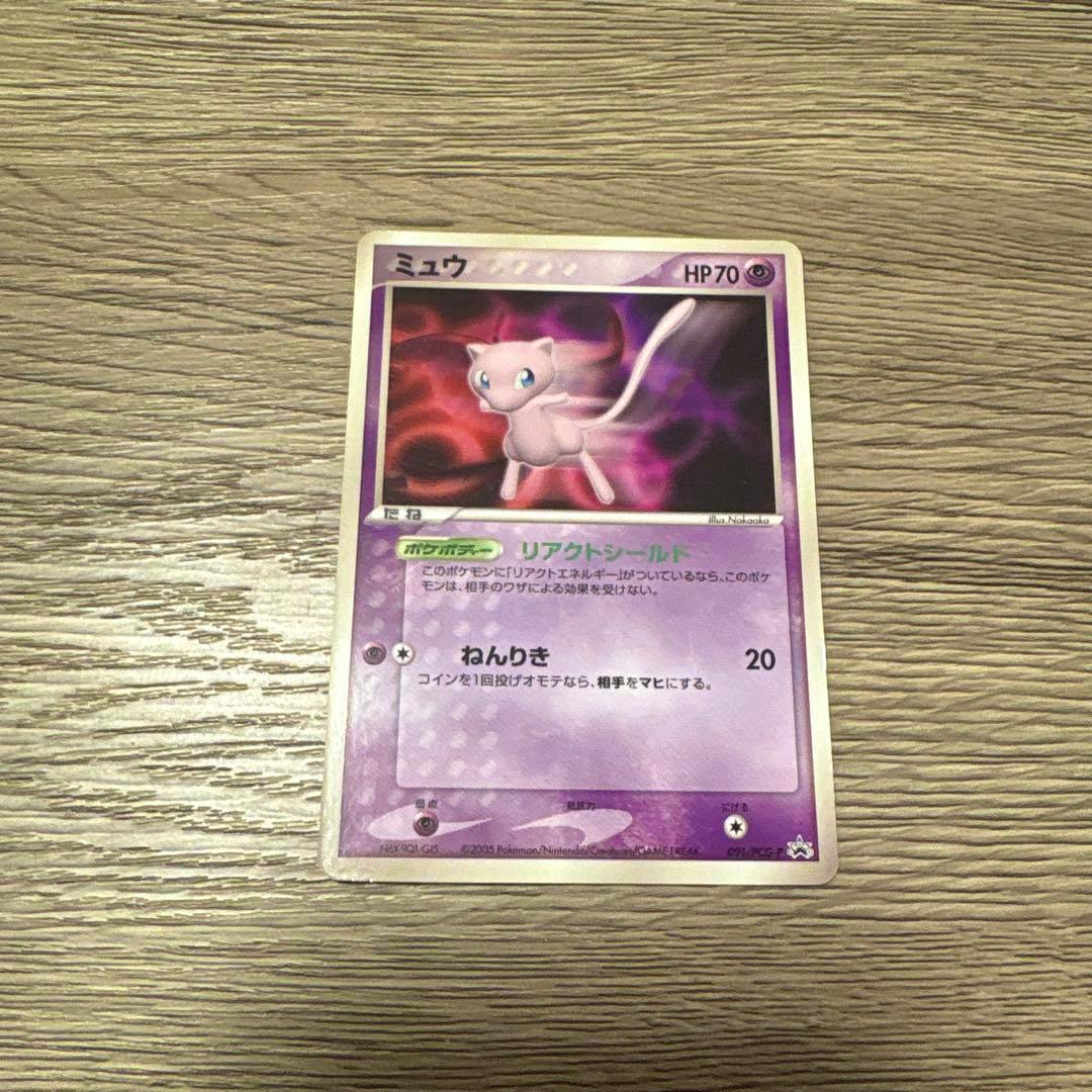Photograph of the front of the ポケモンカード ミュウ プロモ 091/PCG-P trading card lying on a wood surface.