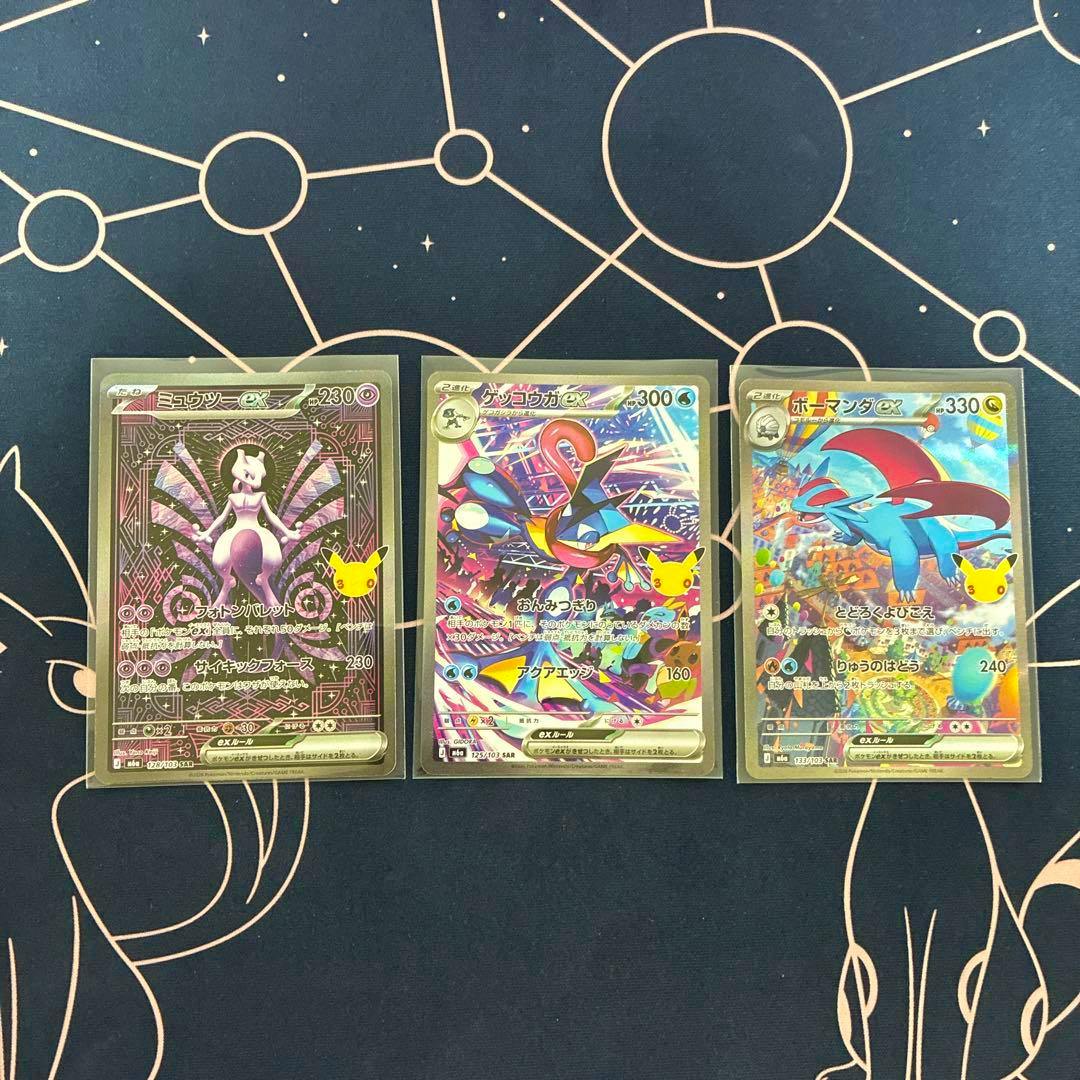 Three Pokémon trading cards (Mewtwo-ex, Greninja-ex, and Salamence-ex) in sleeves laid out on a dark playmat.