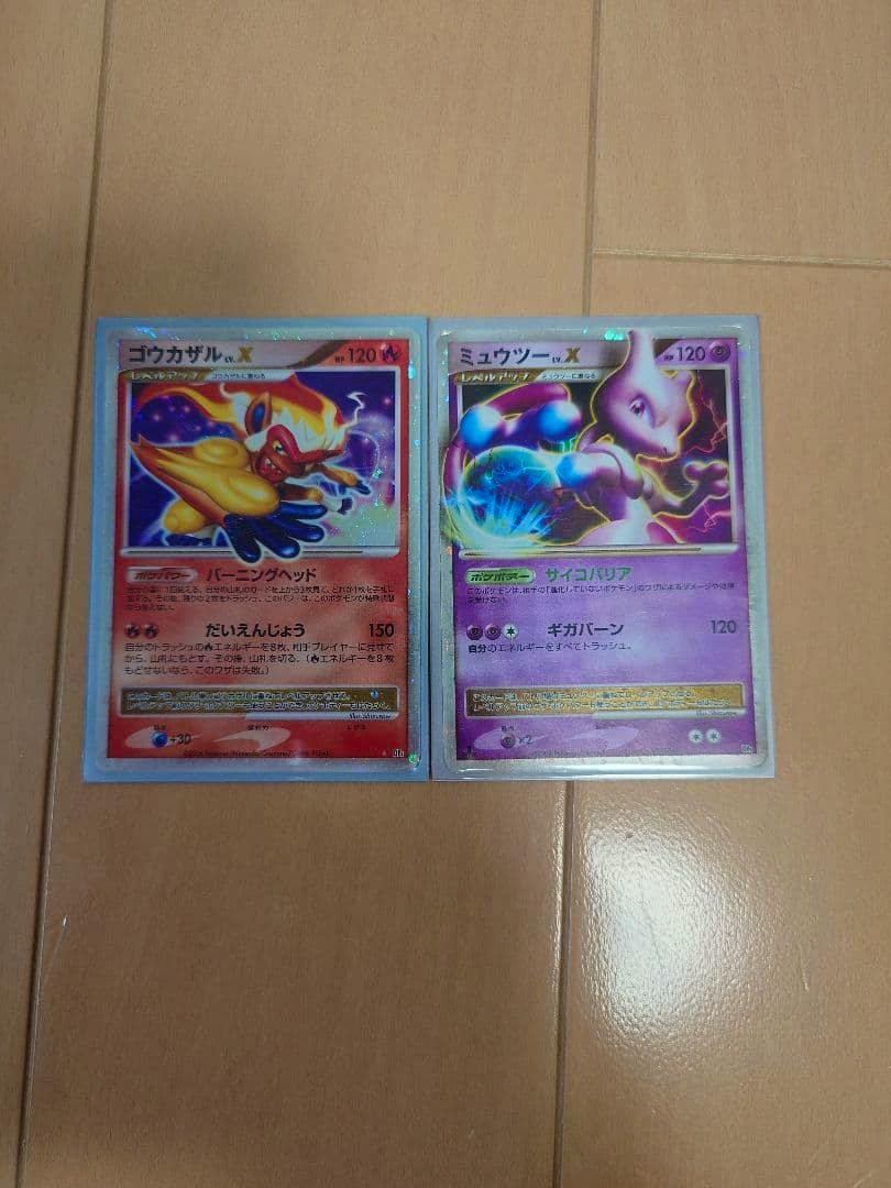 Two Pokémon trading cards, ミュウツーLV.X (right) and ゴウカザルLV.X (left), shown front-facing in clear sleeves on a wooden floor.