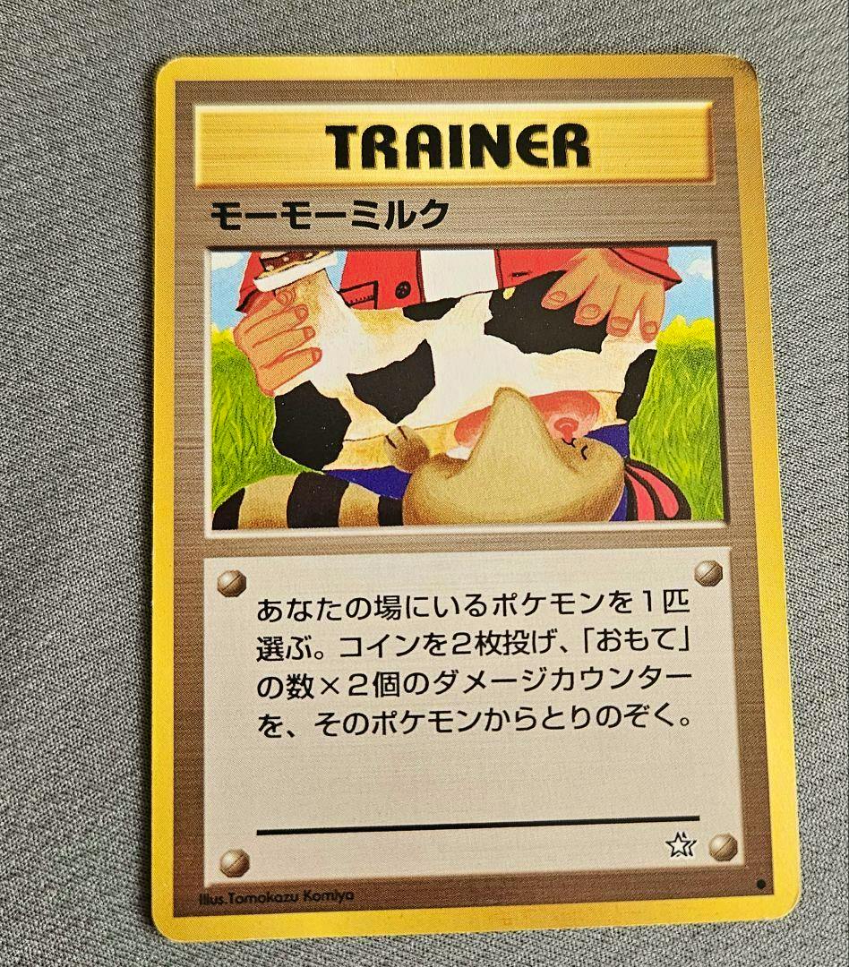 Front view of the Pokémon Trainer card モーモーミルク (MooMoo Milk) placed on gray fabric.