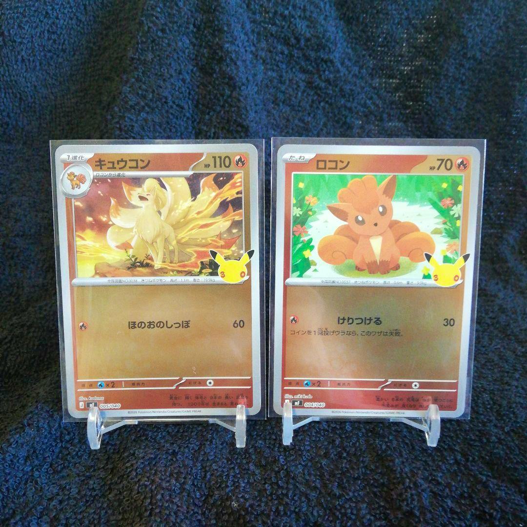 Two Pokémon trading cards (キュウコン and ロコン) in sleeves displayed on clear stands against a dark fabric background.