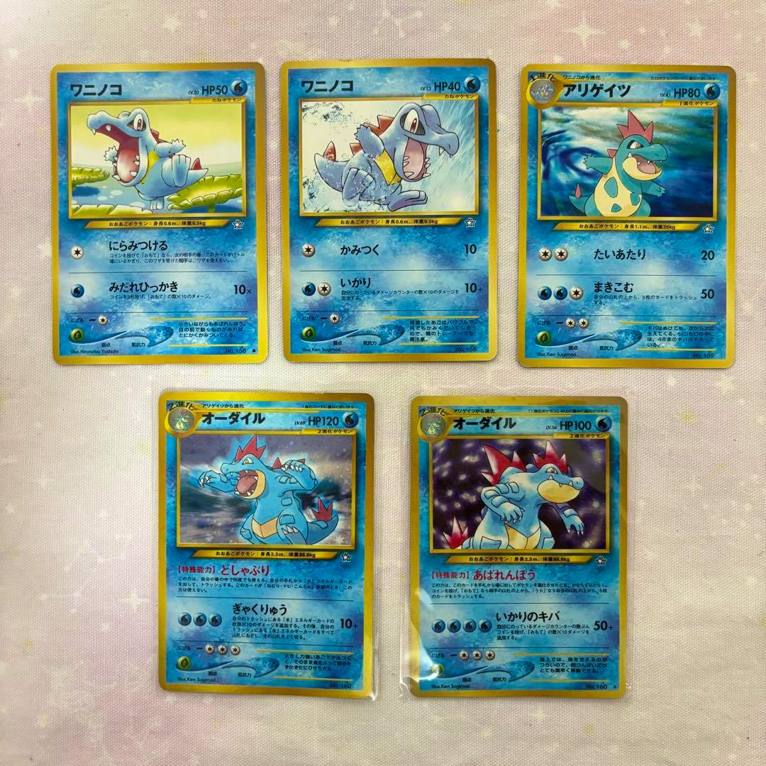 Five old-back Japanese Pokémon trading cards (ワニノコ, アリゲイツ, オーダイル) arranged on a pink fabric background.