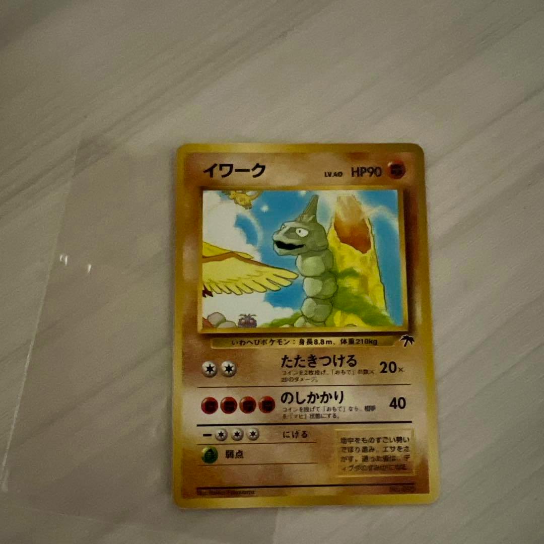 Photograph of the Pokémon trading card "イワーク" in a clear sleeve lying on a light wood surface.