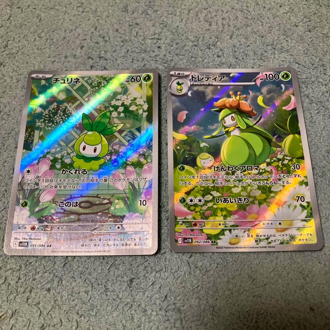 Two Pokémon trading cards (チュリネ and ドレディア) with holographic foil shown side by side on a textured surface.