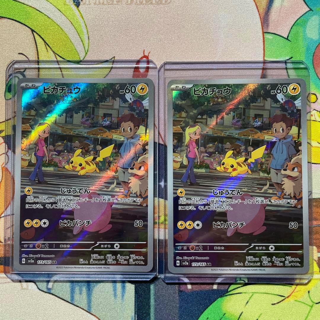 Two Pikachu AR trading cards in protective sleeves shown side by side on a colorful surface.
