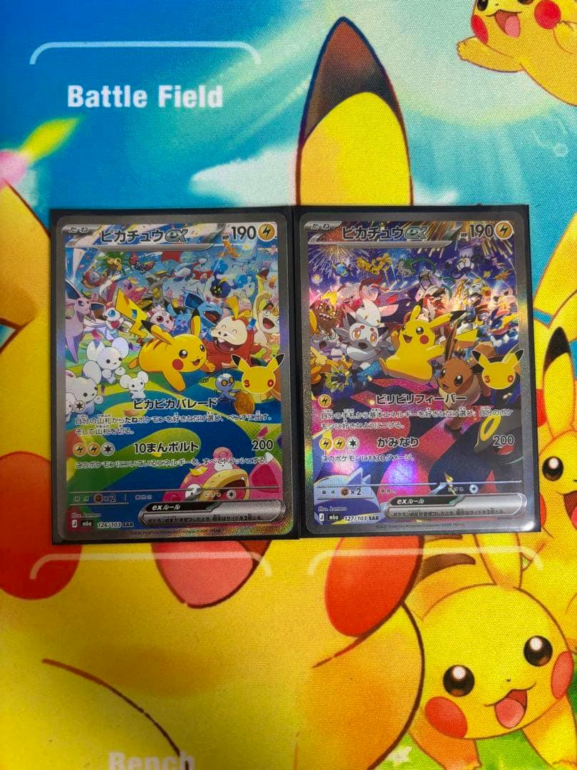 Two holographic Pikachu ex trading cards in sleeves shown side-by-side on a Pikachu playmat.