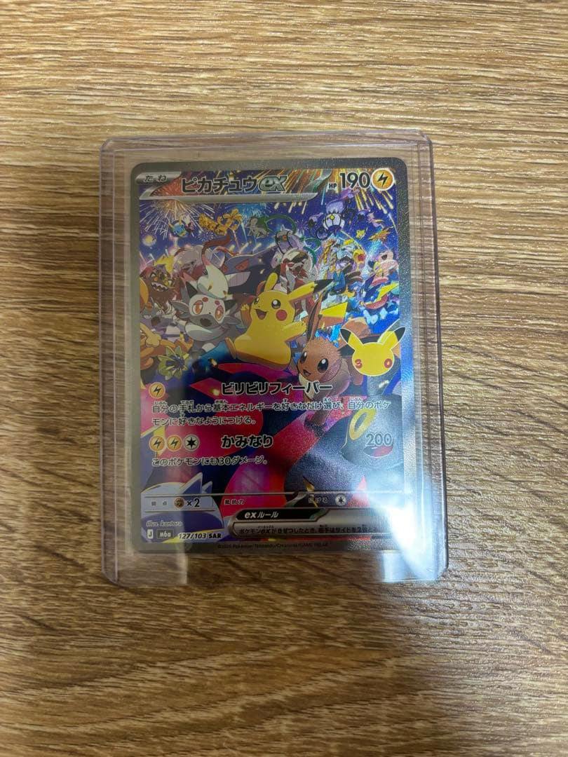 Front of the Pikachu ex SAR (127/103) Pokémon trading card in a plastic sleeve on a wooden surface.