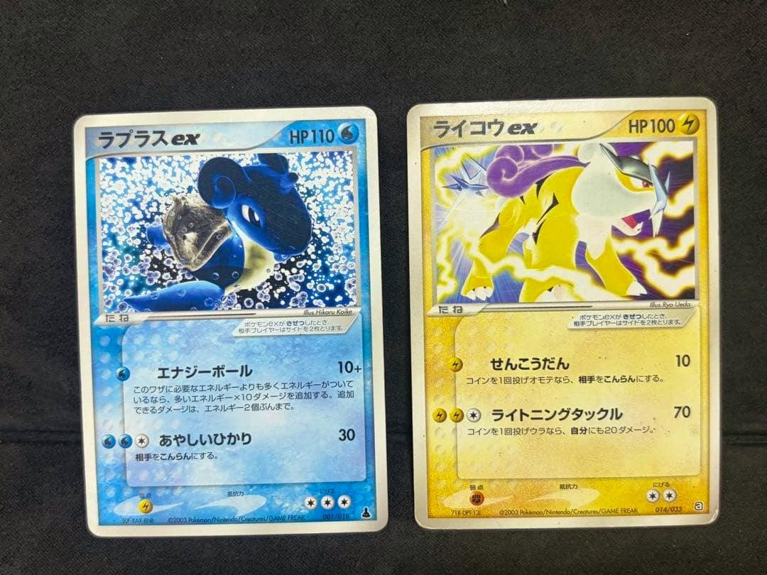 Two Pokémon trading cards (Lapras ex and Raikou ex) placed side by side on a black surface.