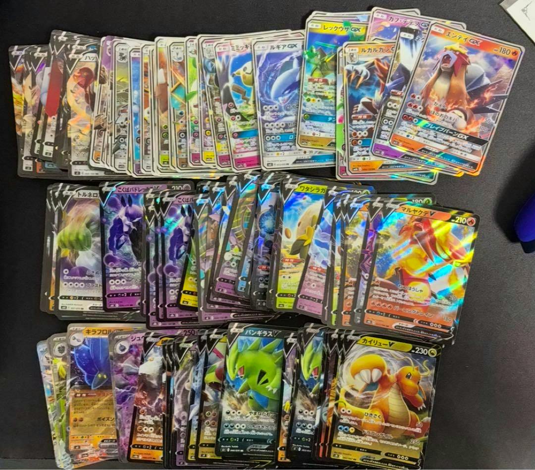 A spread of Pokémon trading cards laid out in rows on a dark surface showing multiple holographic and full-art cards.
