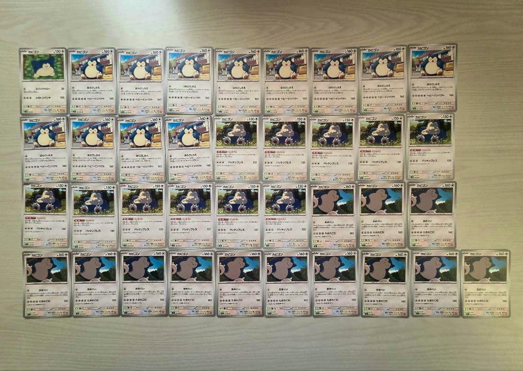 A grid of Pokémon Snorlax trading cards laid out on a light wood surface.