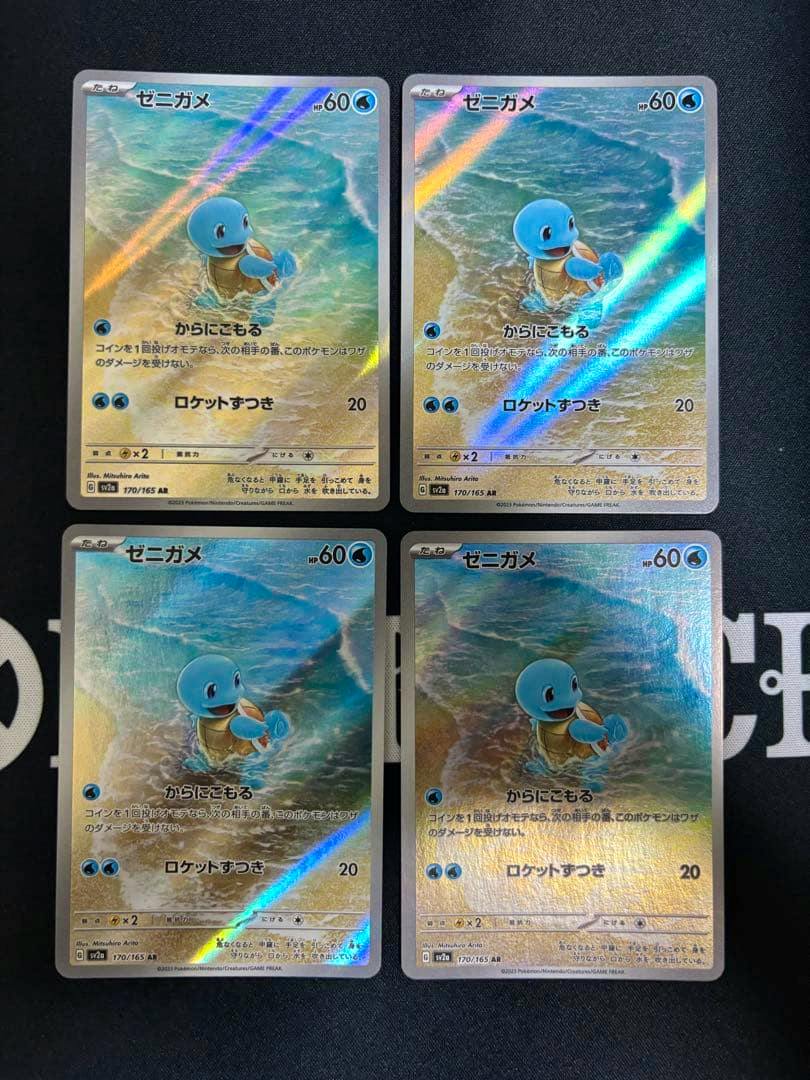 Four holographic Squirtle (ゼニガメ) Pokémon trading cards arranged in a 2x2 grid on a dark surface.