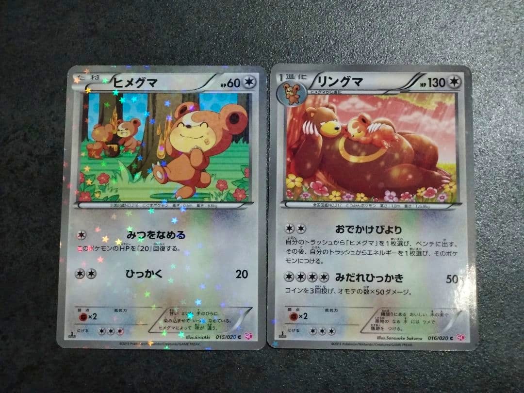 Two Pokémon trading cards (ヒメグマ and リングマ) shown side by side with holographic star foil on a dark surface.