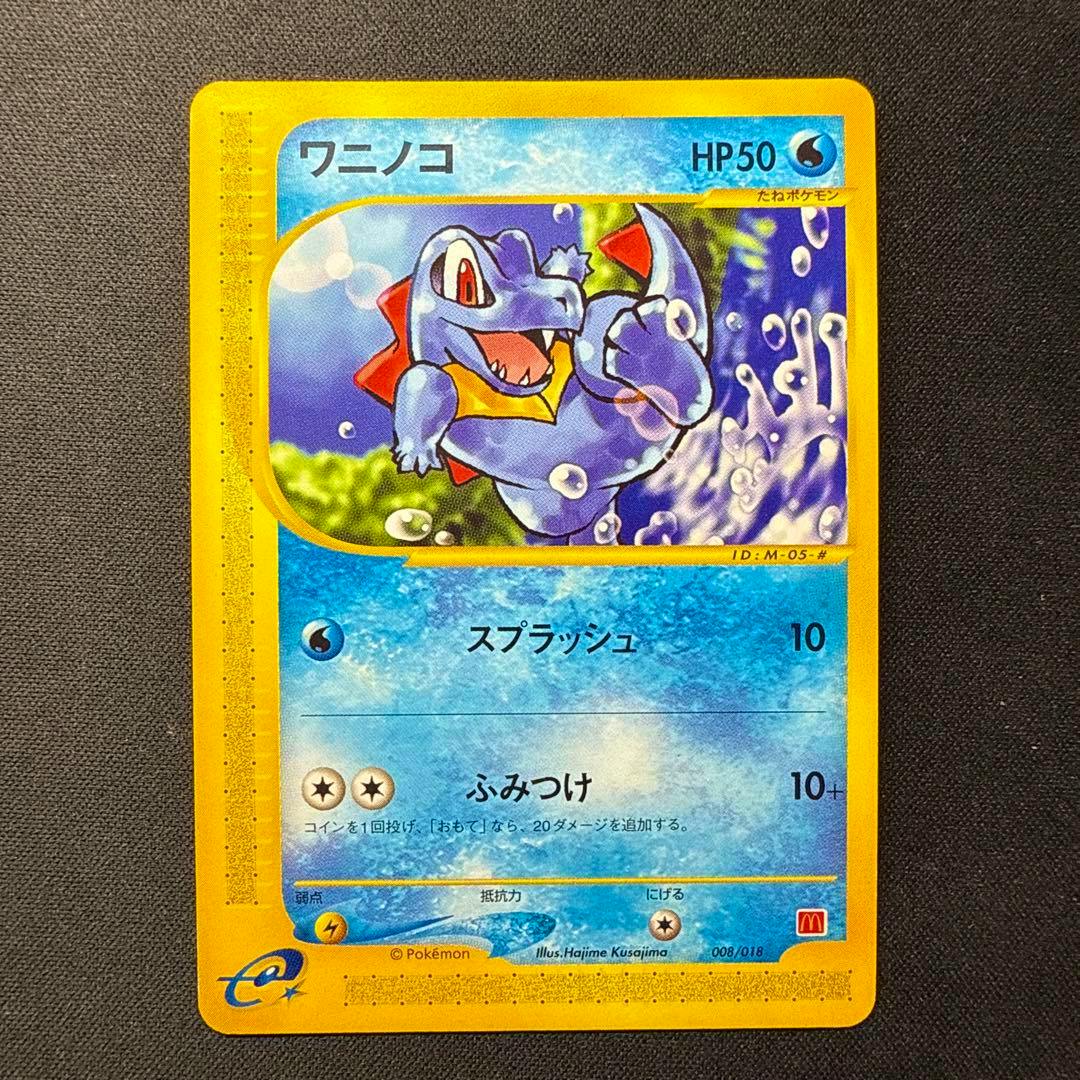 Photograph of the front of the ワニノコ マクドナルドオリジナル ミニマム★パック 008/018 trading card resting on a dark textured background.