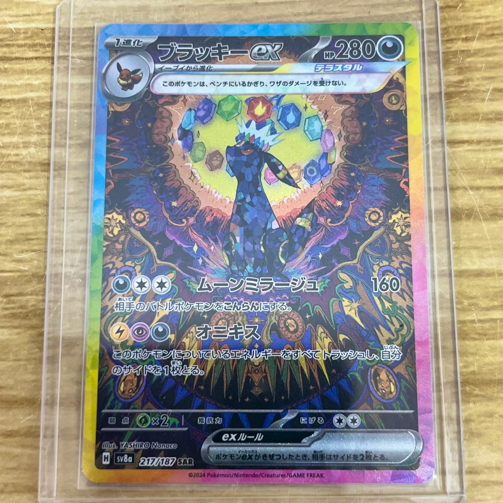 Close-up photo of the front of the ブラッキーex Pokémon trading card (217/187 SAR) in a plastic sleeve on a wooden surface.