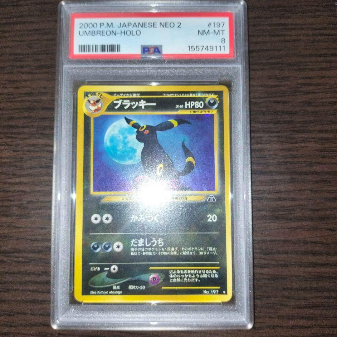 PSA-graded (PSA8) Japanese Umbreon (ブラッキー) Neo 2 holo trading card in a hard plastic slab resting on a wooden surface.