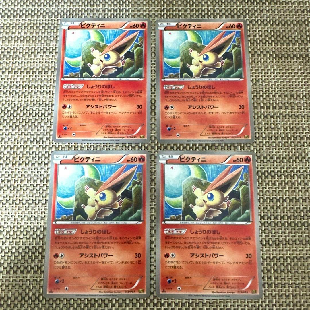 Four Japanese Victini Pokémon trading cards (front) arranged in a two-by-two grid on a woven surface.