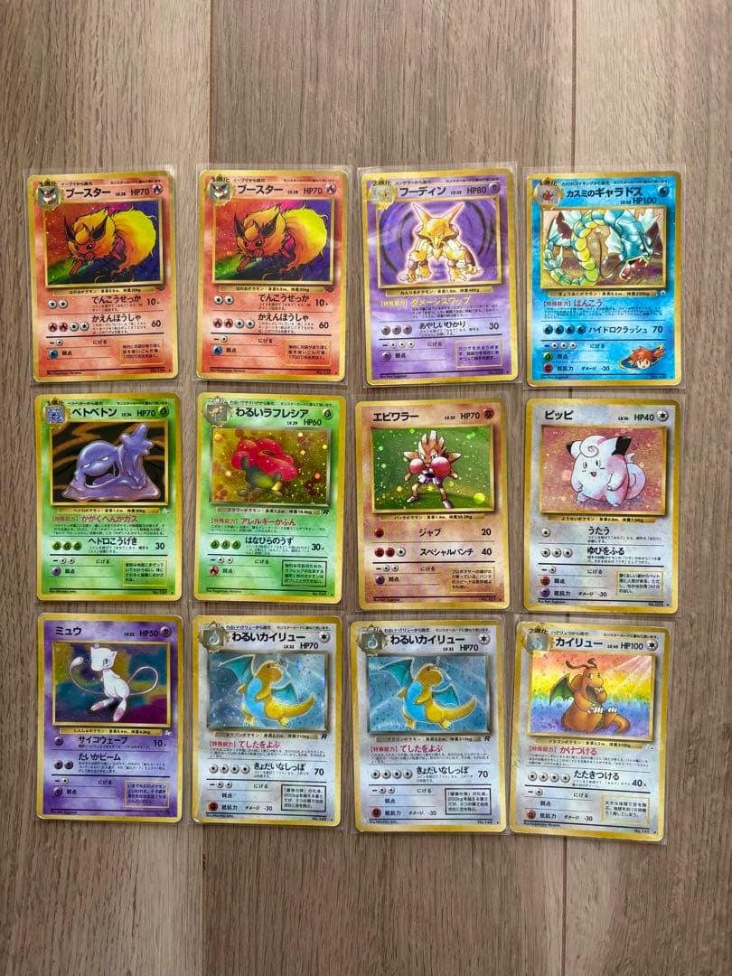 Twelve Pokémon trading cards from the listed old-back holo 12-card set arranged in a 3x4 grid on a wooden floor, showing the card fronts.