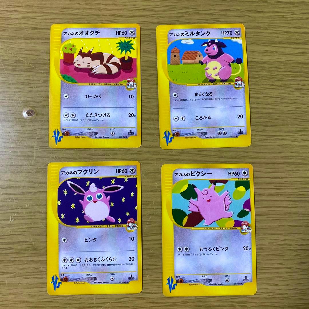 Four Pokémon trading cards face-up on a wooden surface showing アカネのオオタチ, アカネのミルタンク, アカネのプクリン, and アカネのピクシー.