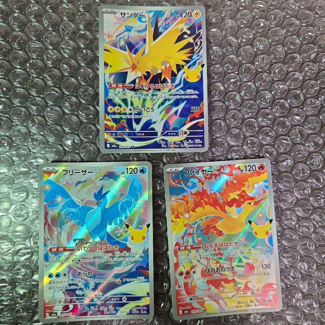 Three Pokémon trading cards (Zapdos, Articuno, and Moltres AR) laid on bubble wrap, showing holographic fronts.