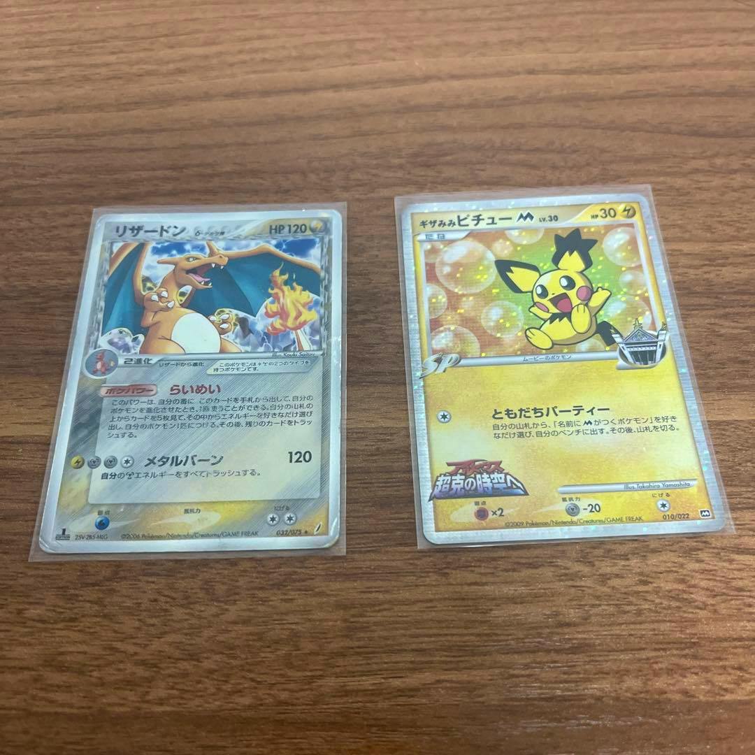 Fronts of two Pokémon trading cards in sleeves, showing Charizard on the left and Pichu on the right on a wooden surface.