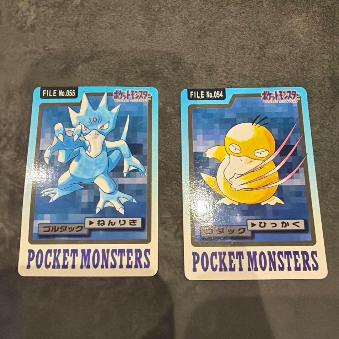 Two Pocket Monsters Carddass photocard cards showing Golduck (left) and Psyduck (right) laid side by side on a gray surface.