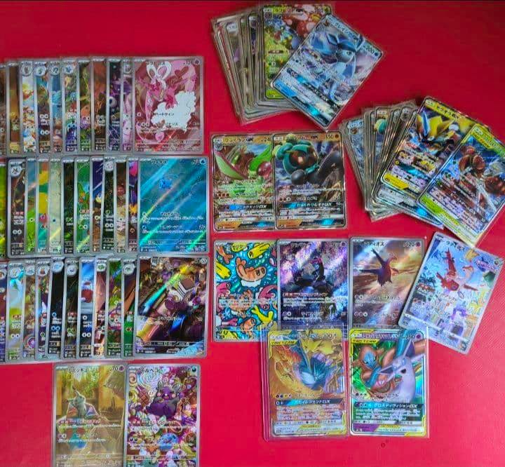 Many Pokémon trading cards laid out on a red background, showing various holographic and full-art cards.