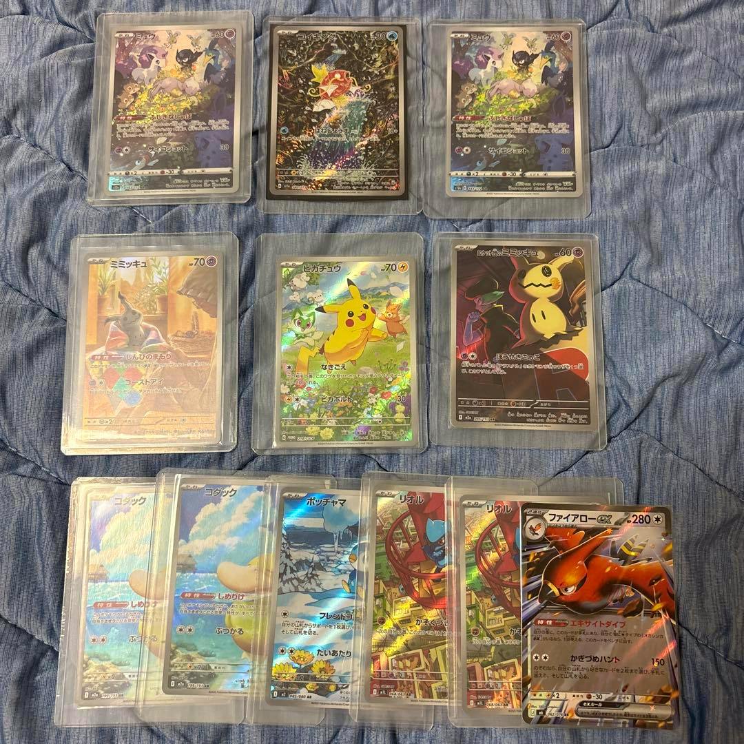 Eleven Pokémon trading cards in protective sleeves laid out on a blue fabric background, including several holographic AR cards.