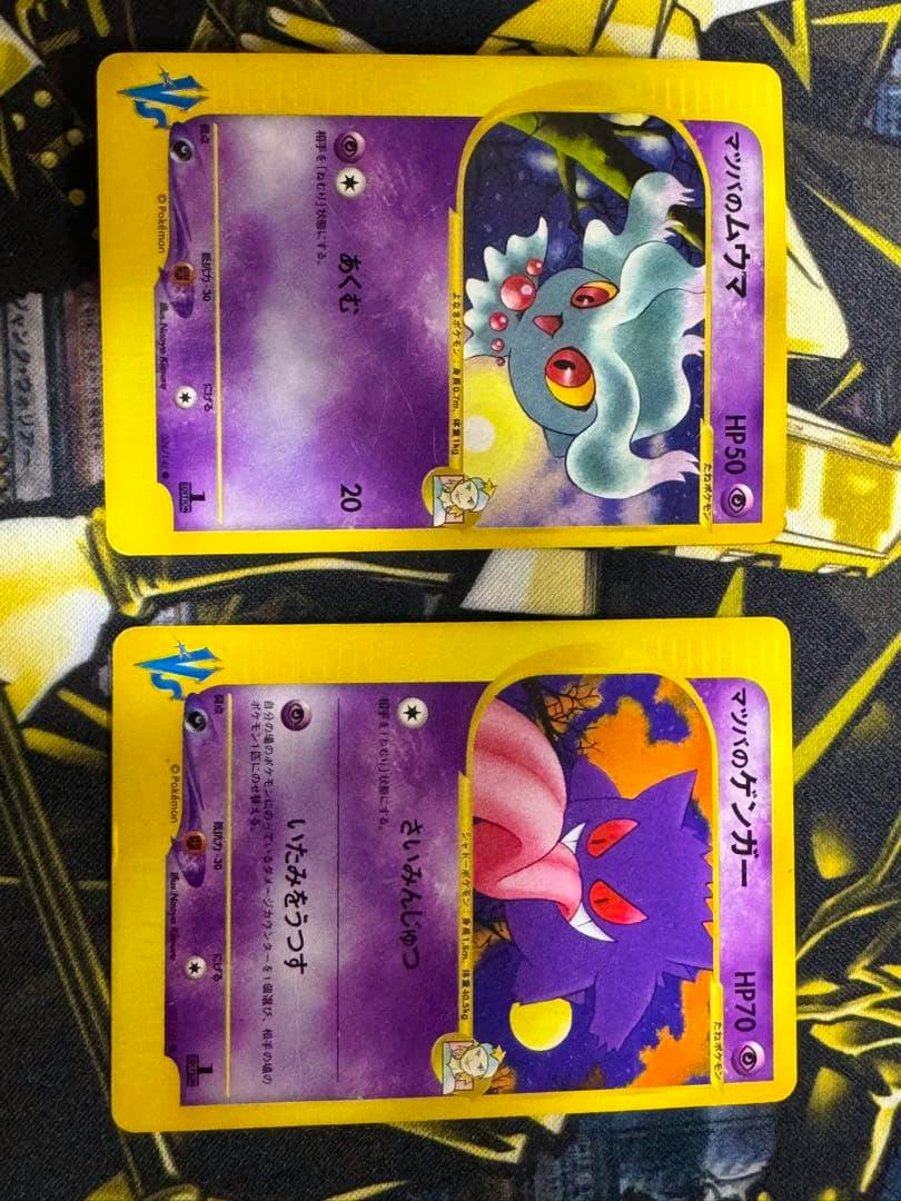 Photo of two Pokémon trading cards (マツバのゲンガー and ムウマ) lying on a patterned cloth, both cards visible.