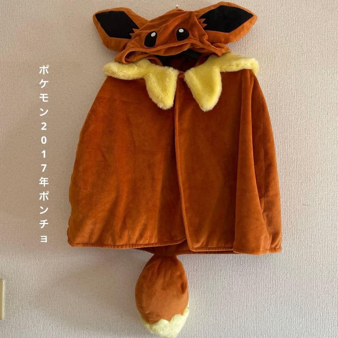 Brown hooded Pokémon-themed women's poncho with a yellow fur collar and attached tail hanging on a wall, front view.