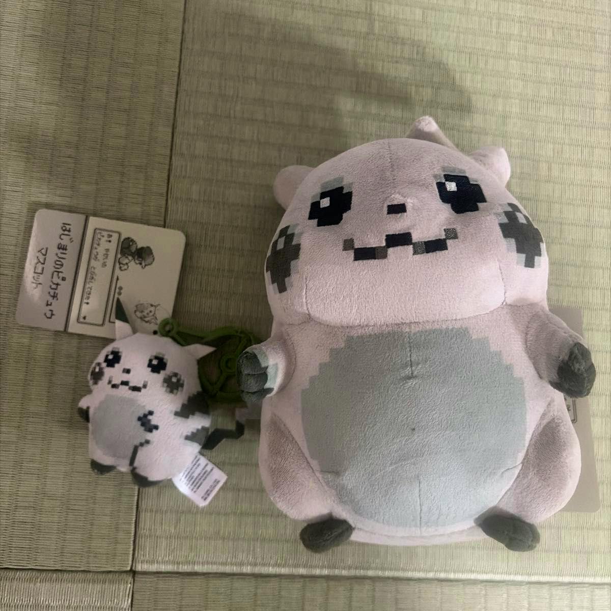 Two Pikachu plush mascots (a larger plush and a small keychain plush) displayed on a tatami mat with tags visible.