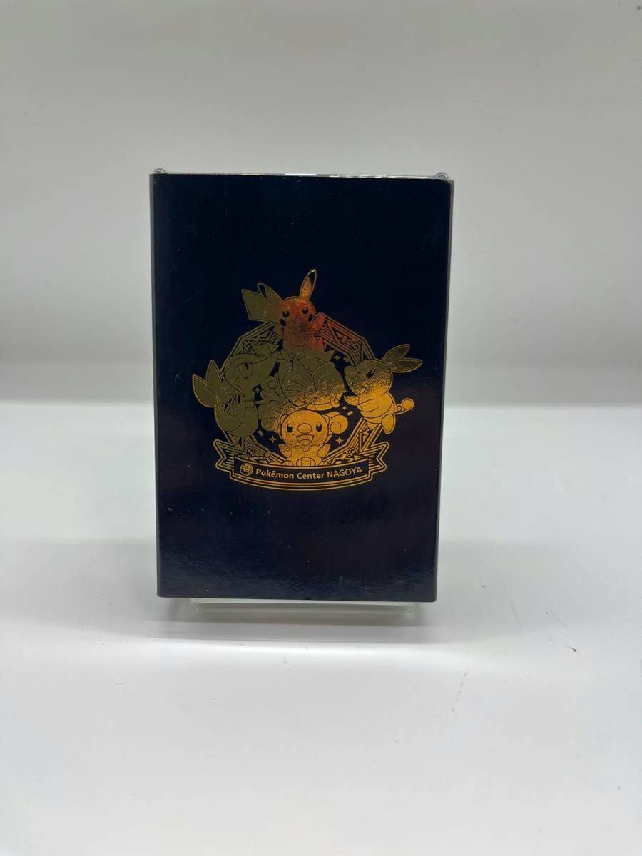 Black playing card box with a gold Pokémon Center NAGOYA emblem standing upright on a white background.