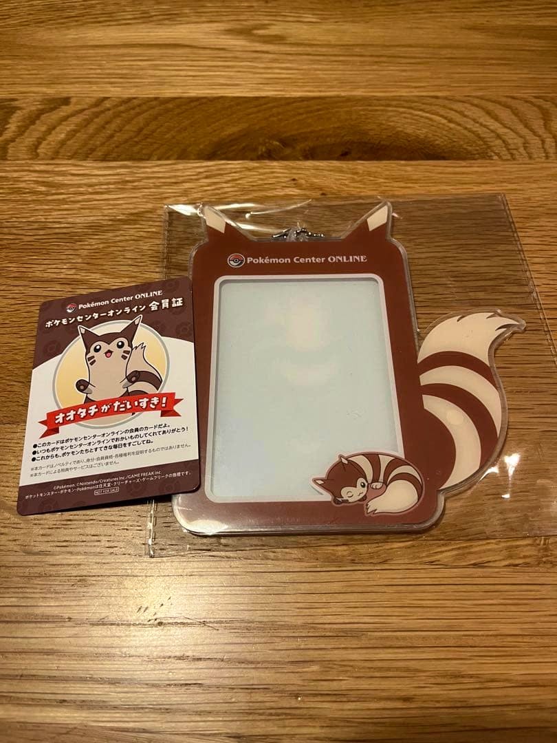 A Furret-themed brown acrylic card case in plastic packaging shown on a wooden surface with a Pokémon Center Online membership card next to it.