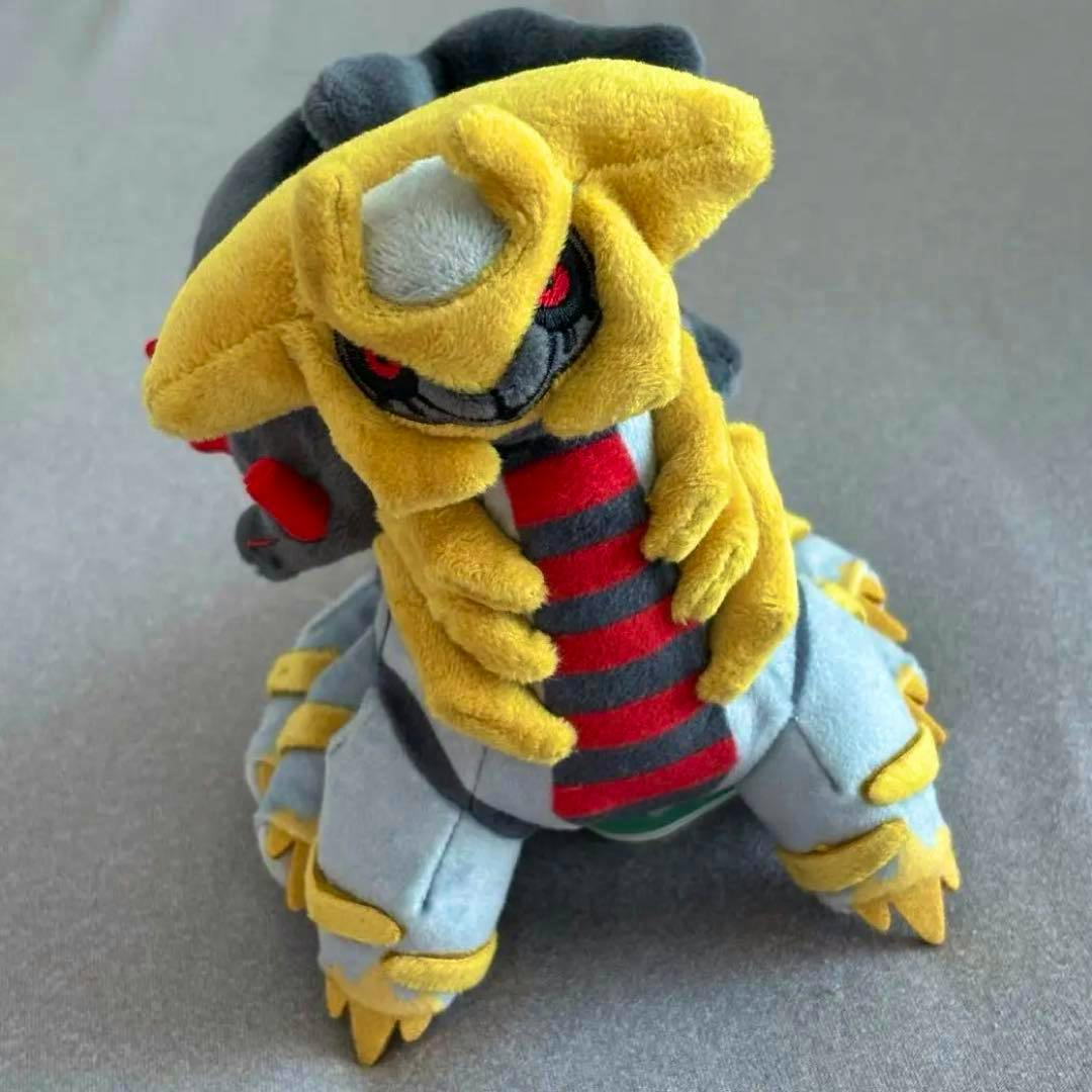 Front-angle photo of a Giratina (Another Forme) Pokémon Center fit plush sitting on a gray surface.