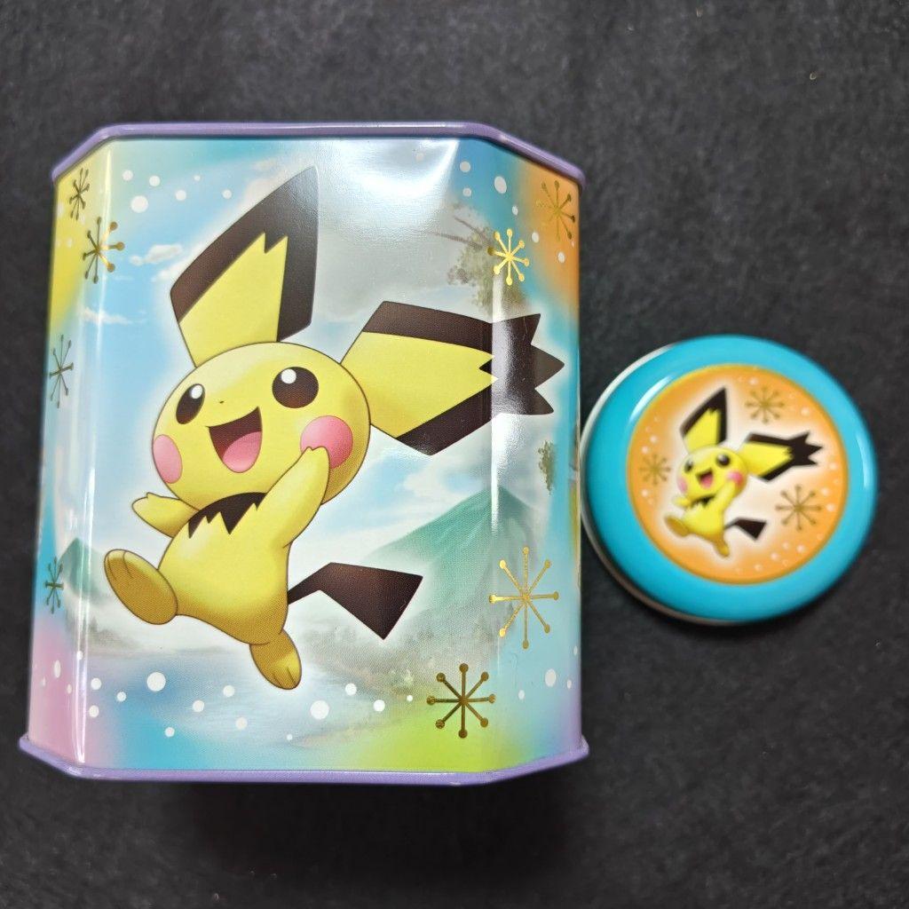 A tin candy box decorated with a jumping Pichu and its round lid shown beside it.