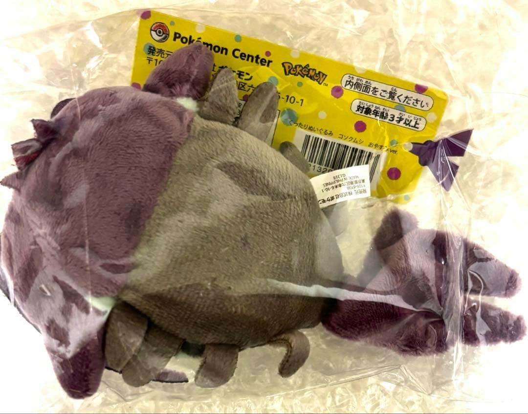 A Pokémon Center コソクムシ plush inside clear plastic packaging showing the plush from the back with the yellow Pokémon Center tag visible.