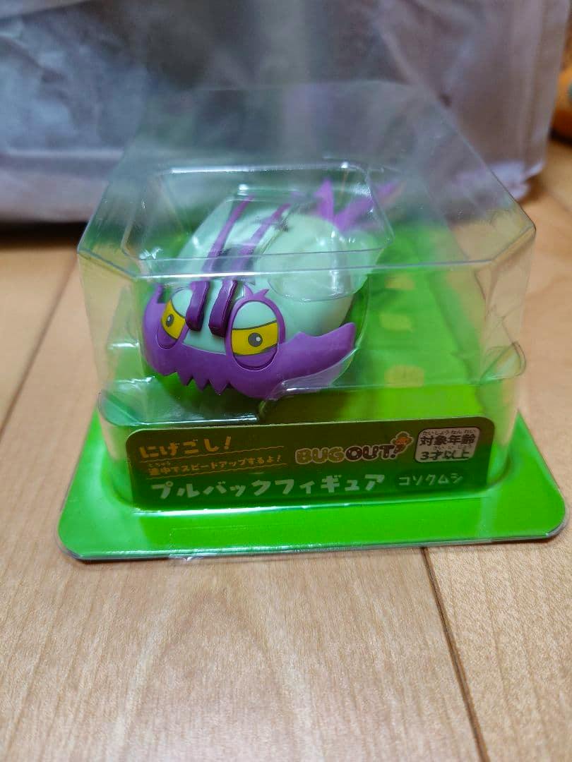 Pull-back plastic figure of コソクムシ (Pokémon) shown in clear plastic blister packaging on a green backing.
