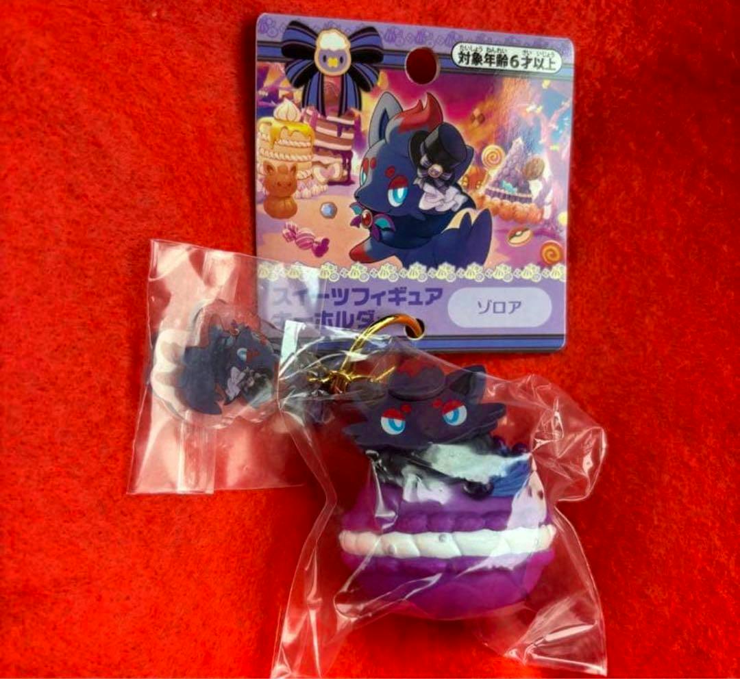 A packaged plastic Zorua Halloween sweets figure keychain with its illustrated backing card on a red background.