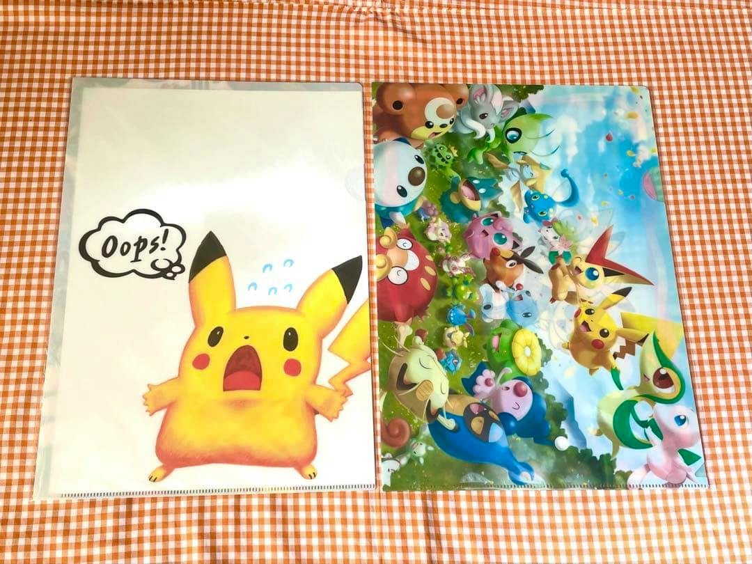 Two Pokémon clear files laid flat on an orange gingham cloth, one showing a surprised Pikachu design and the other a colorful group-of-Pokémon scene.
