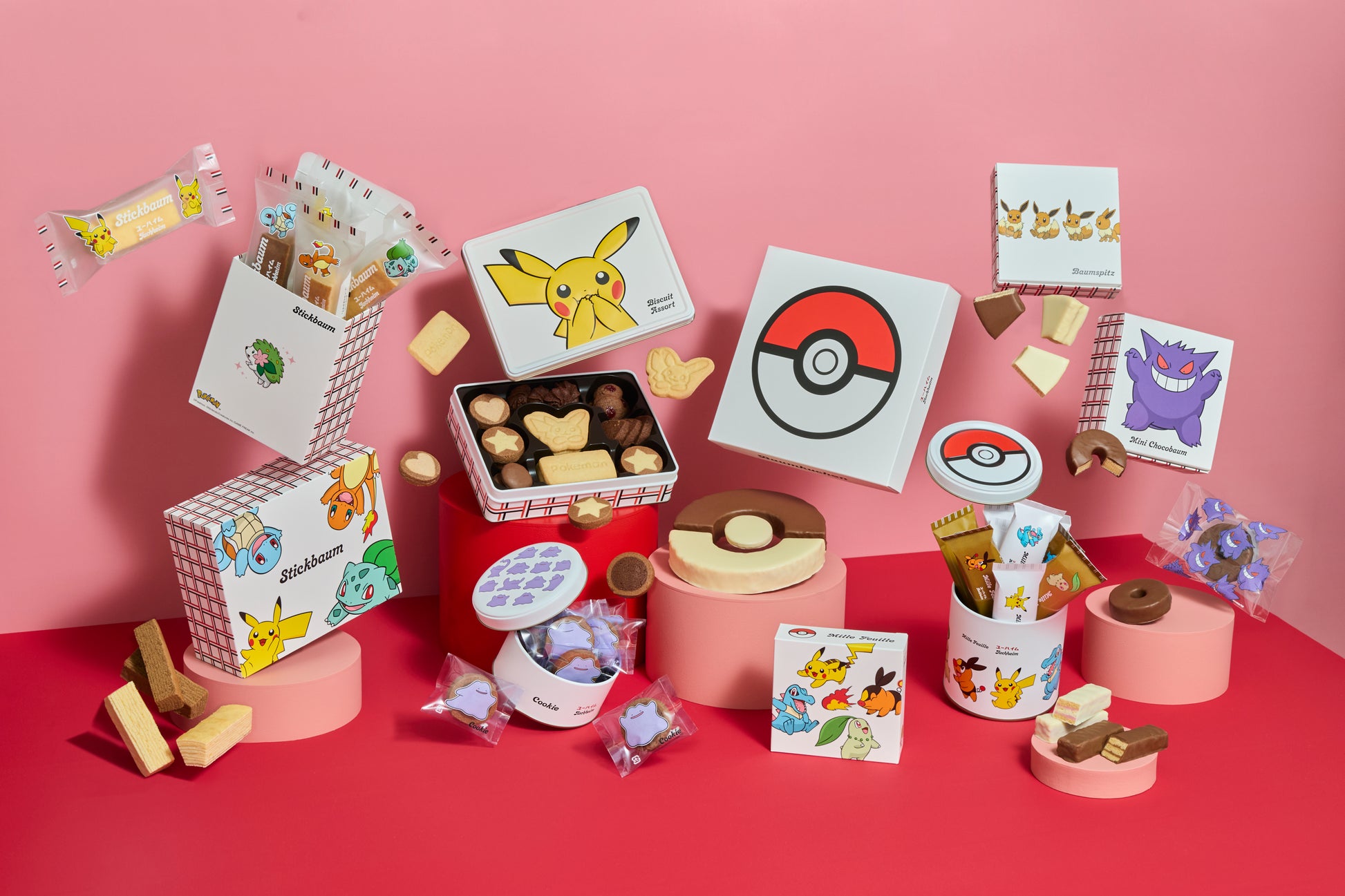 Pokémon-themed boxes, tins, and individually wrapped filled chocolate snacks arranged on a pink background.