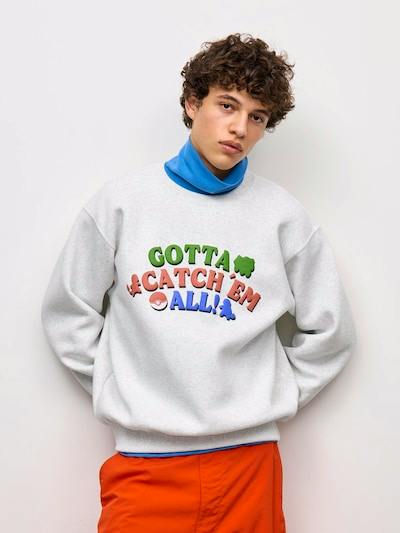 Male model wearing a light gray Pokémon sweatshirt with a colorful "GOTTA CATCH 'EM ALL!" graphic on the front.