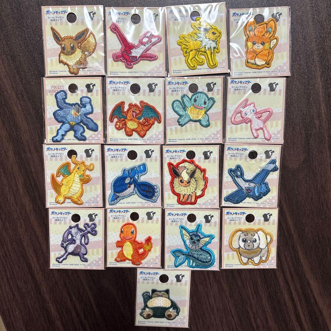 Packaged Pokémon embroidered fabric patches from the listed set arranged in a grid on a dark wood surface.