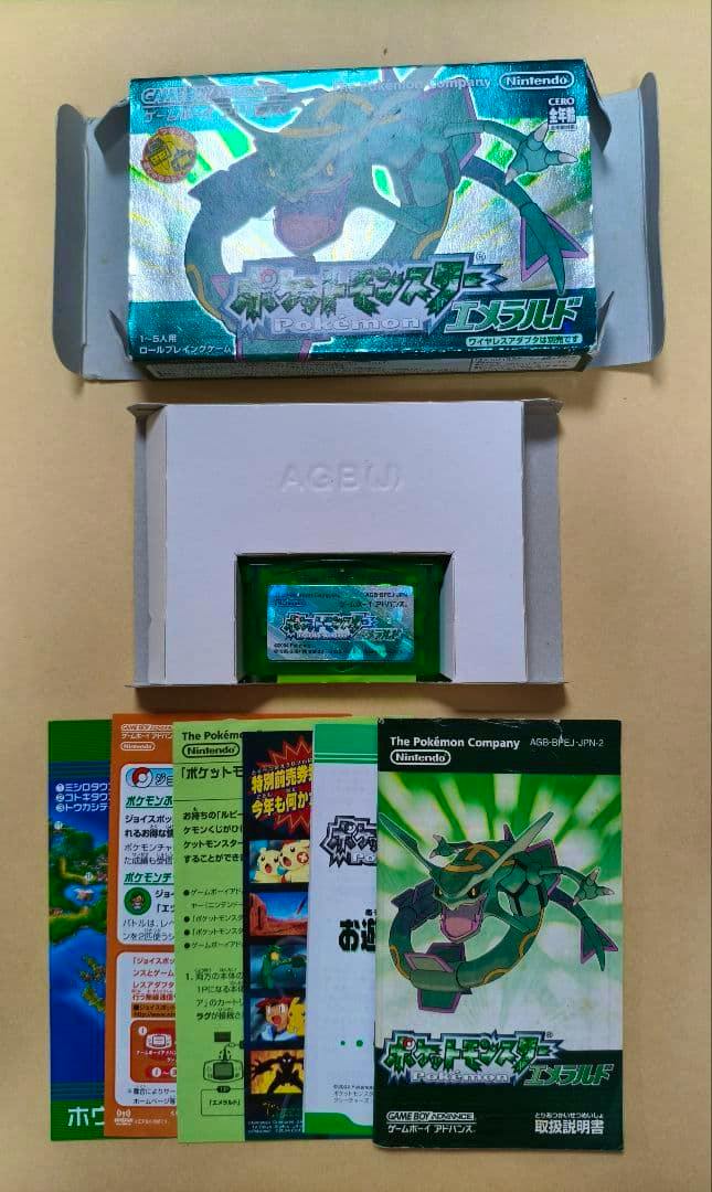 Game Boy Advance Pokémon Emerald cartridge in its inner tray with the outer box and several instruction booklets laid out on a surface.