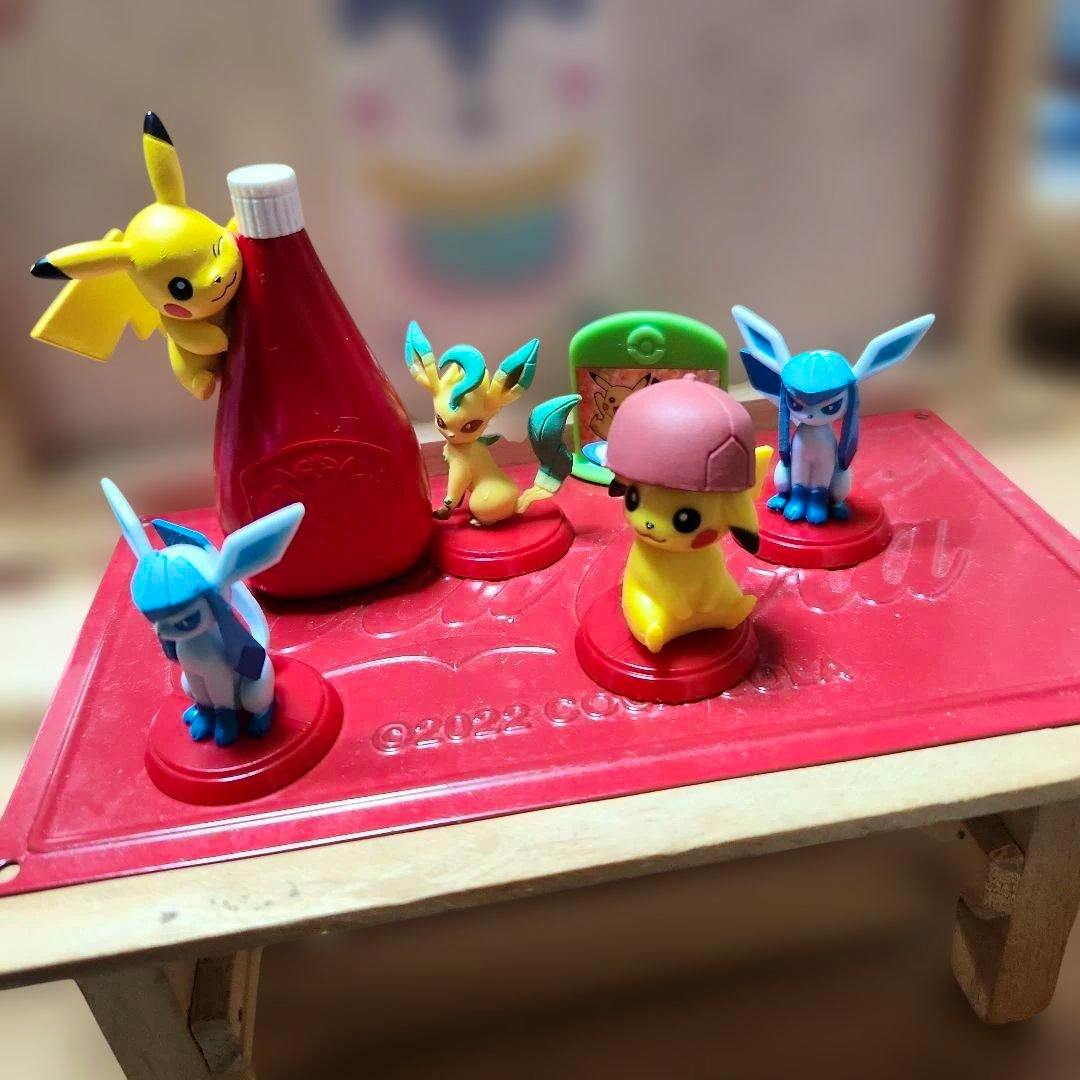 Small plastic Pokémon figures displayed on a red tray, featuring a Pikachu wearing a pink hat in front.