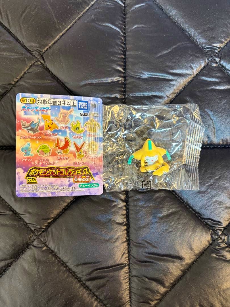 A small Jirachi plastic figure sealed in clear packaging displayed next to its colorful product card.