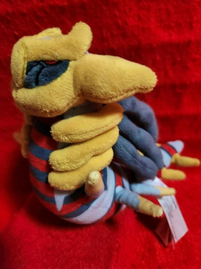 Side view of a Giratina plush toy showing yellow and gray features on a red background.