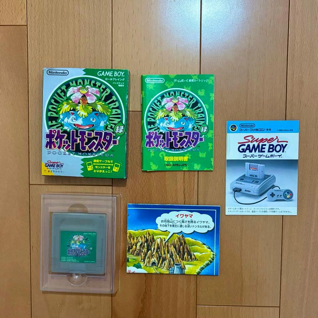 Pocket Monsters Green Game Boy cartridge, its green box, instruction manual, and inserts arranged on a wooden floor.