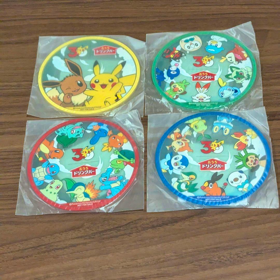 Four round Pokémon coasters in individual plastic sleeves arranged on a wooden surface.