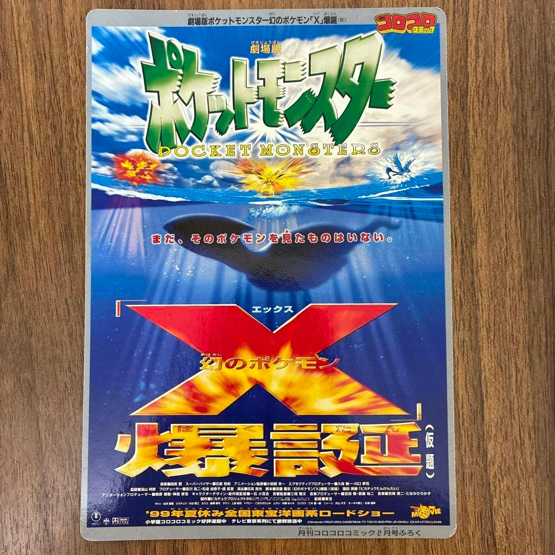 Photo of the art board showing Pocket Monsters movie artwork with Lugia and a large red X logo on a wooden surface.